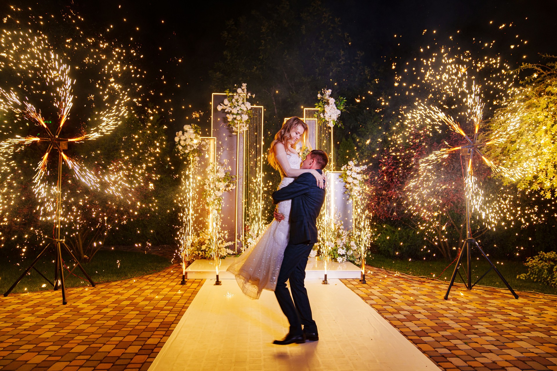 The bride and groom on the wedding ceremony venue with fireworks at night .