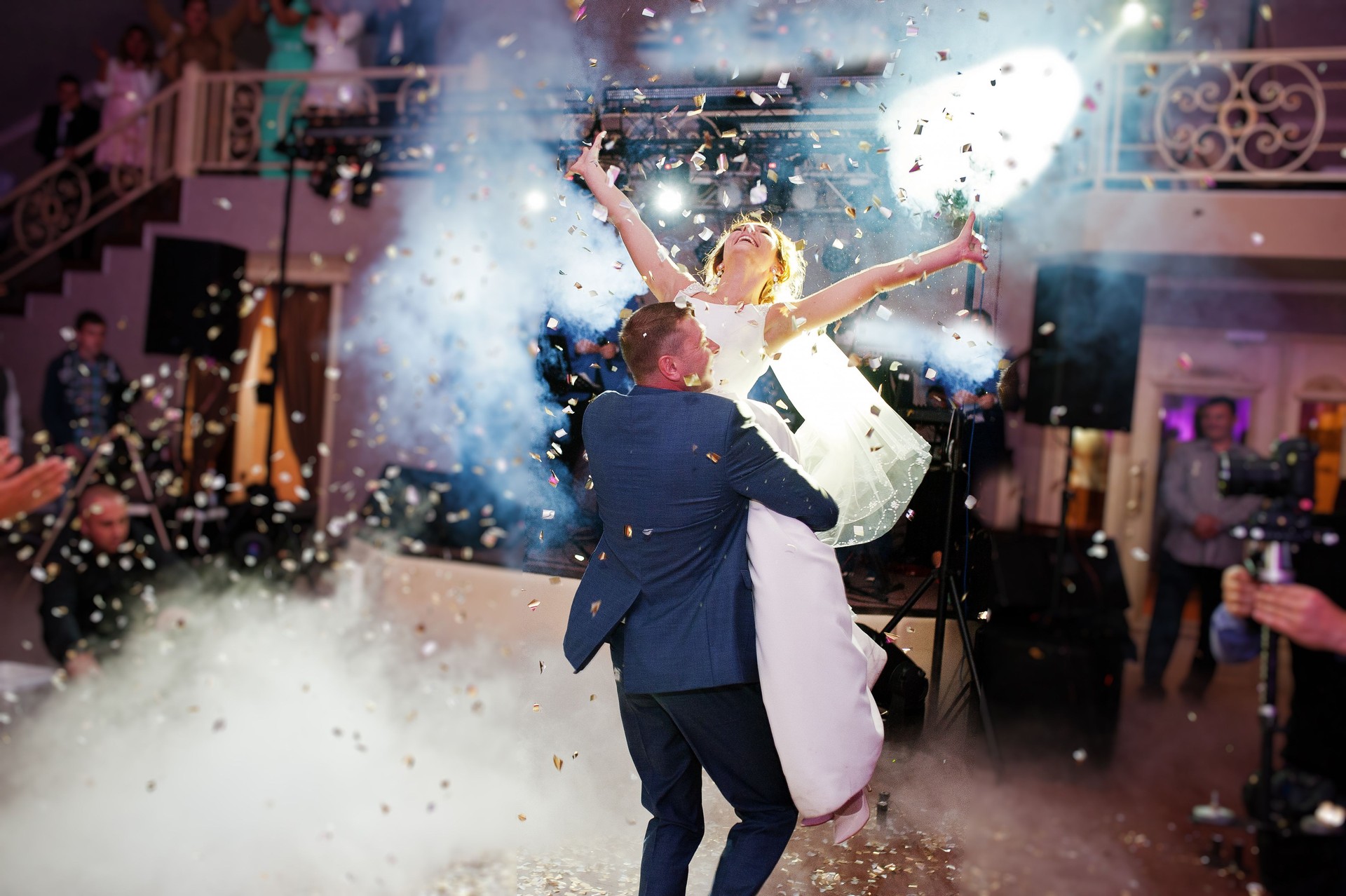 Newly married couple dancing on their wedding party with heavy smoke and multicolored lights on the background.